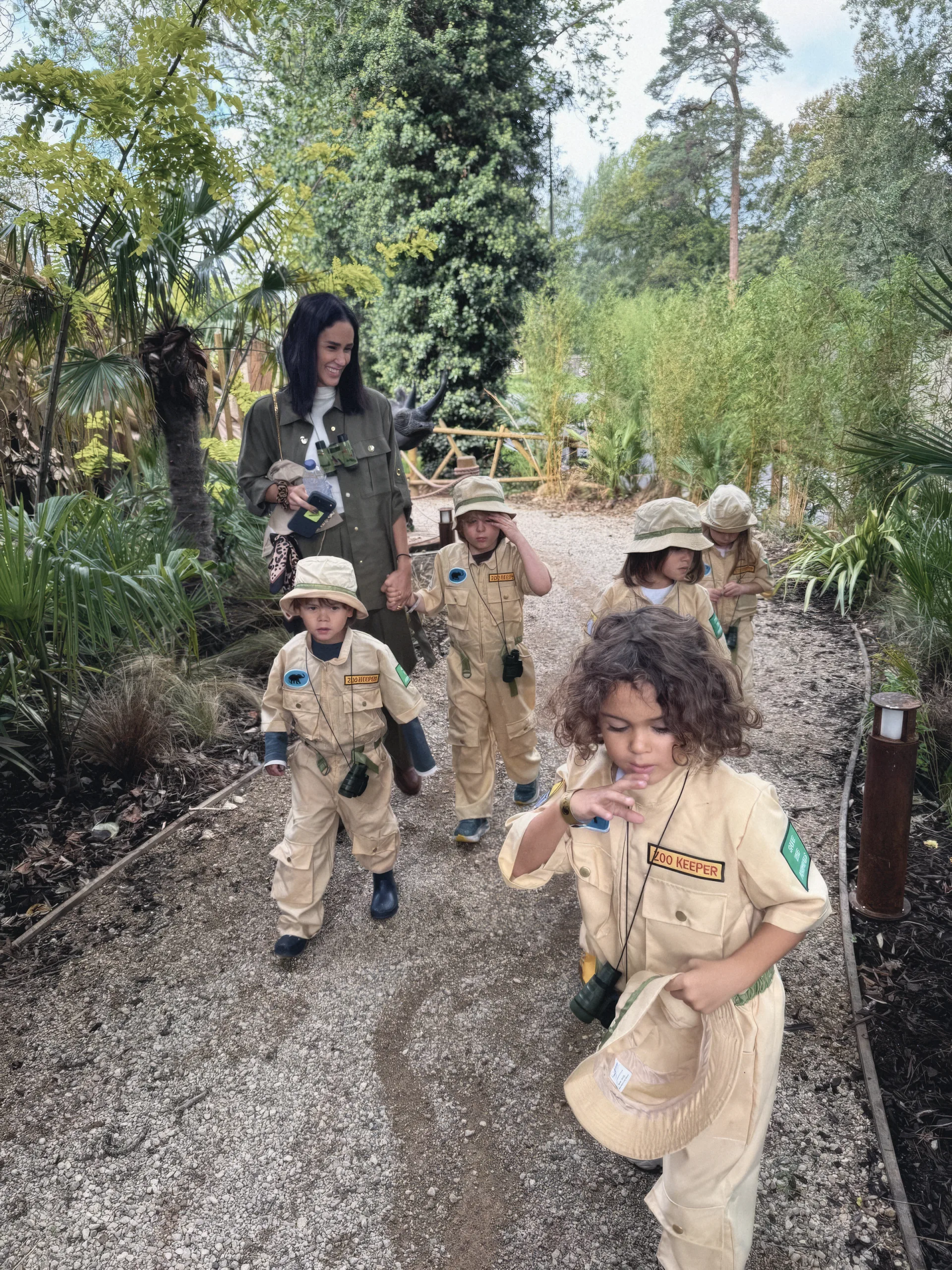 Maria leading a group of children in safari outfits along a forest path